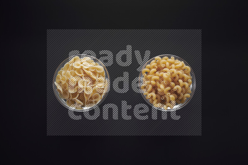 Different pasta types in glass bowls on black background