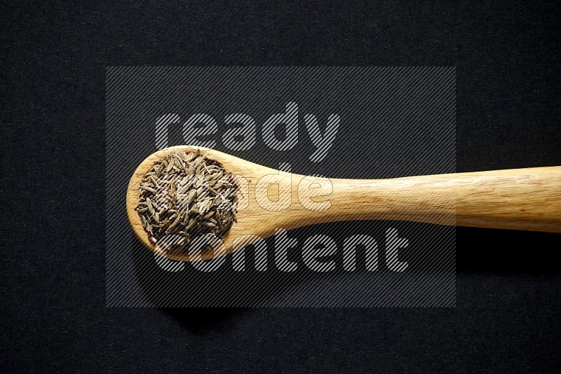 A wooden spoon full of cumin seeds on black flooring