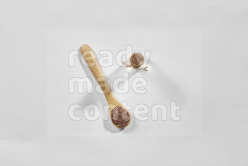 A wooden spoon full of flax seeds and a glass bottle full of flaxseeds oil on a white flooring