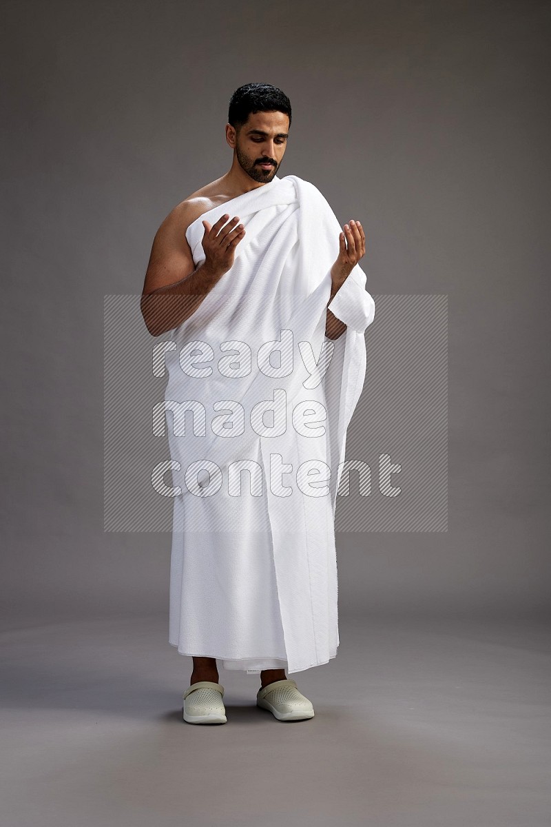 A man wearing Ehram Standing performing dua'a on gray background