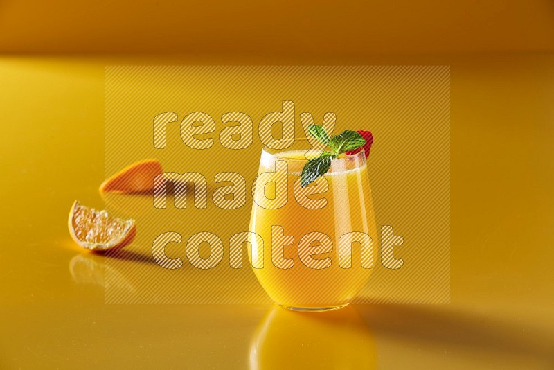 glass of orange juice with berry & mint on yellow background