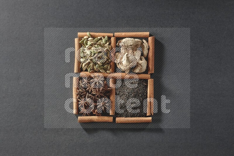 4 مربعات من عيدان القرفة ممتلئة بالشاي واليانسون النجمي والزنجبيل المجفف وحب الهيل على أرضية سوداء