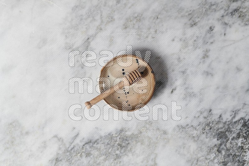 Multicolored Pottery bowl with wooden honey handle in it, on grey marble flooring, Top View