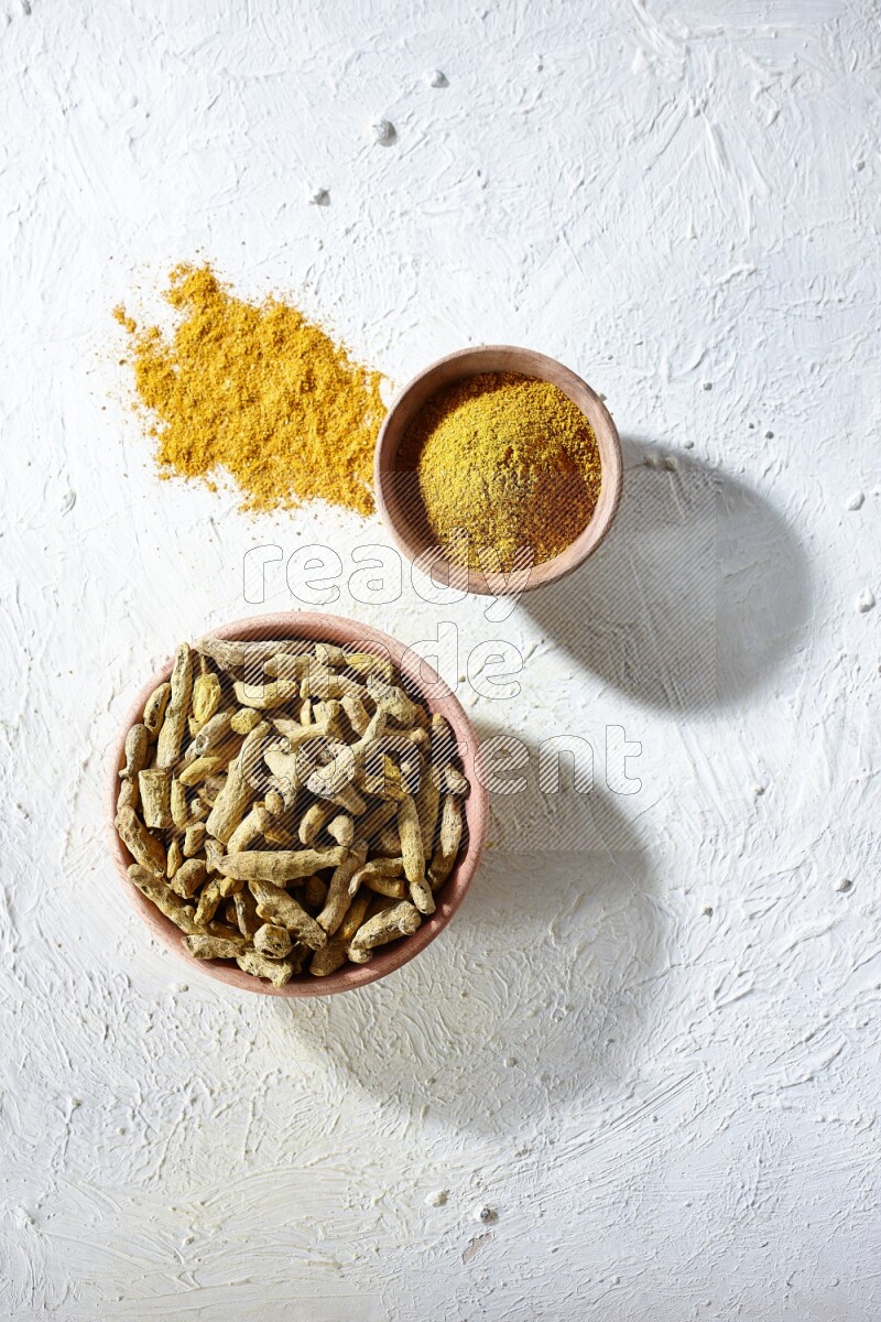 وعاءان خشبيان، أحدهما ممتلئ ببودرة الكركم والآخر بأصابع الكركم المجففة، على خلفية بيضاء