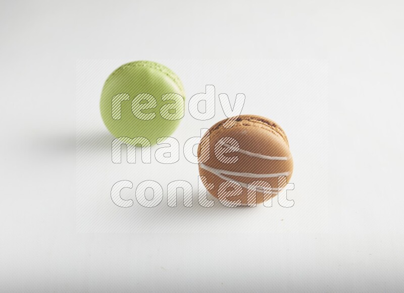 45º Shot of of two assorted Brown Irish Cream, and Green Pistachio macarons on white background