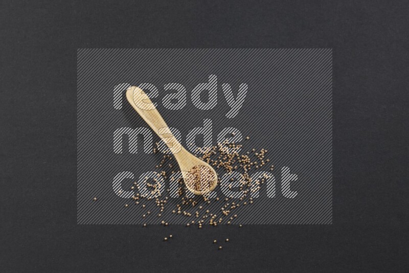 A wooden spoon full of mustard seeds on a black flooring