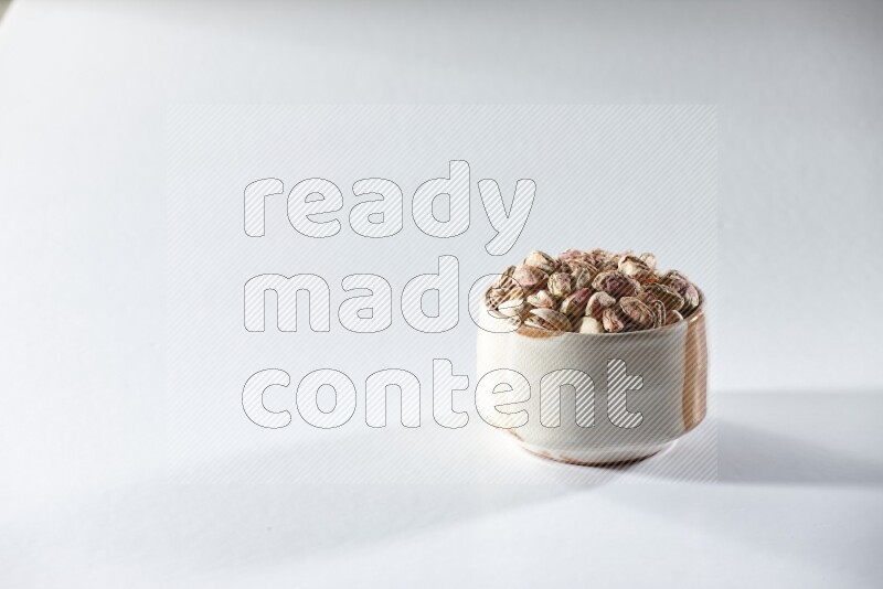 A beige ceramic bowl full of peeled pistachios on a white background in different angles