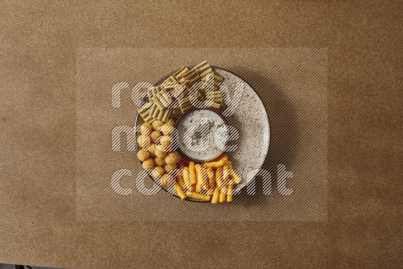 Assorted snacks on a pottery plate with a dipping on brown background