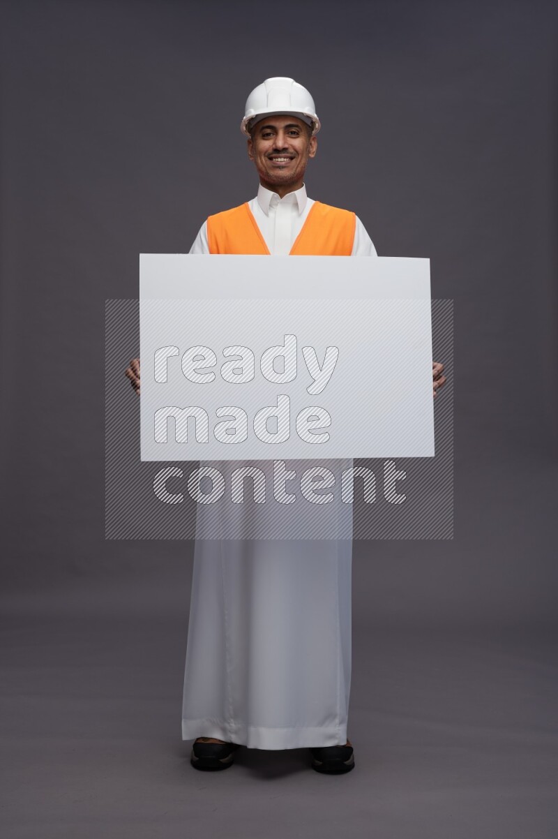 Saudi man wearing thob with engineer vest standing holding board on gray background