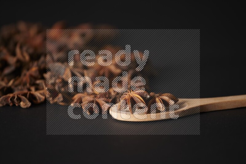 اليانسون النجمي في ملعقة خشبية ومتناثر على أرضية سوداء