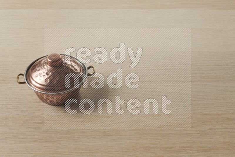 A small copper pot on light wooden background