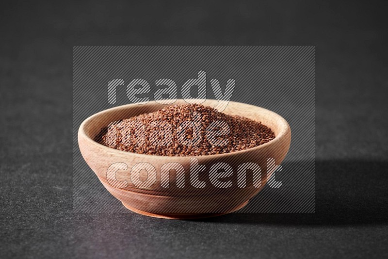 A wooden bowl full of garden cress seeds on a black flooring