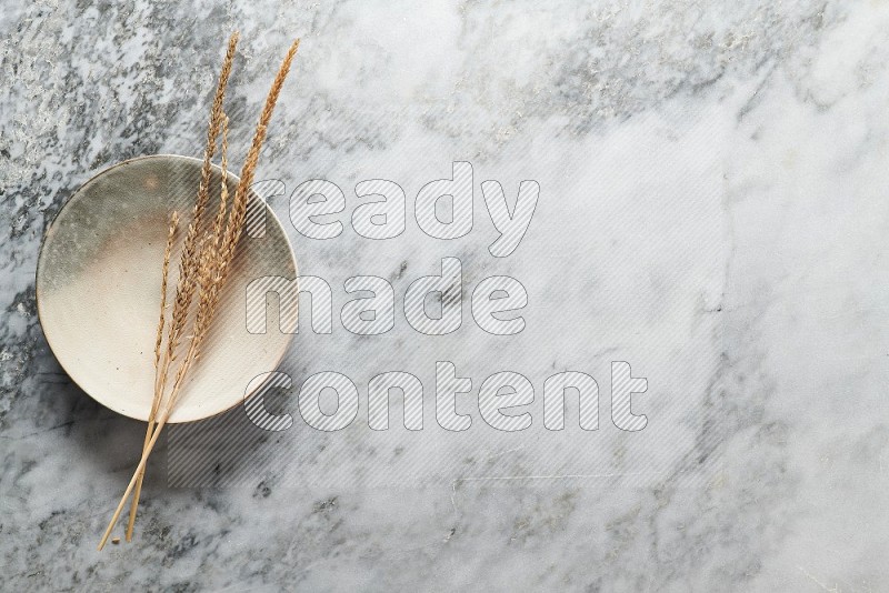 Wheat stalks on Multicolored Pottery Plate on grey marble flooring, Top view