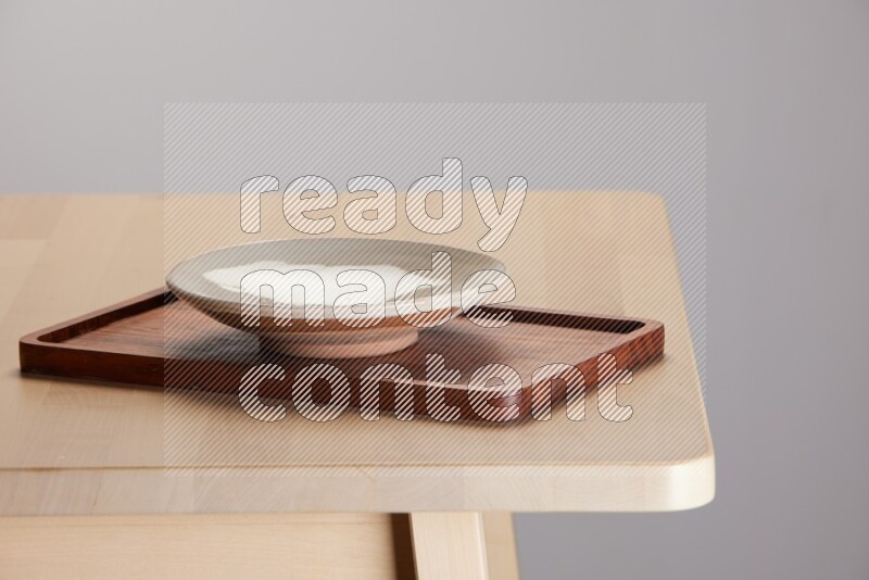 multi-colored pottery Plate placed on a rectangular wooden tray on the edge of wooden table