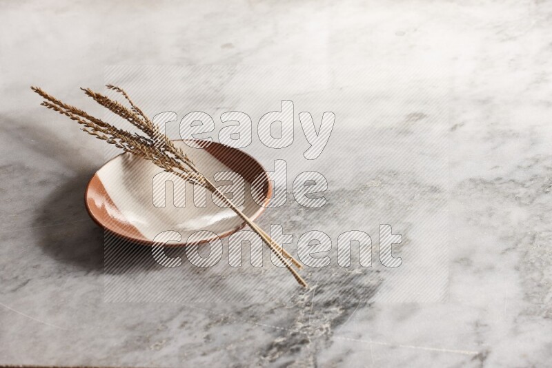 Wheat stalks on multicolored pottery plate on grey marble background
