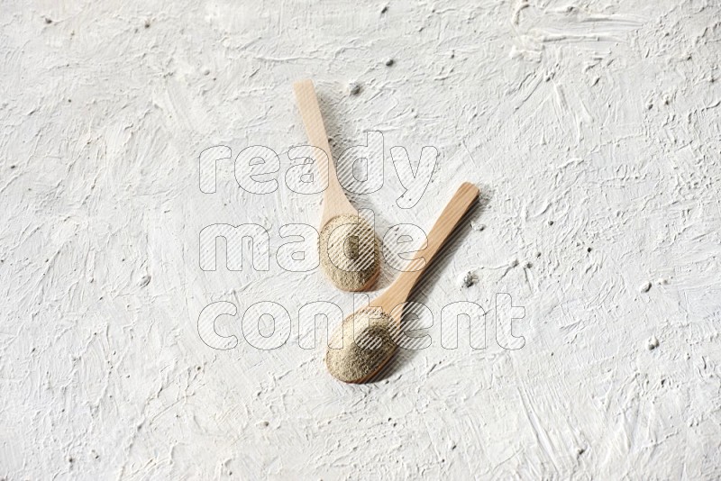 2 wooden spoons full of white pepper powder on textured white flooring