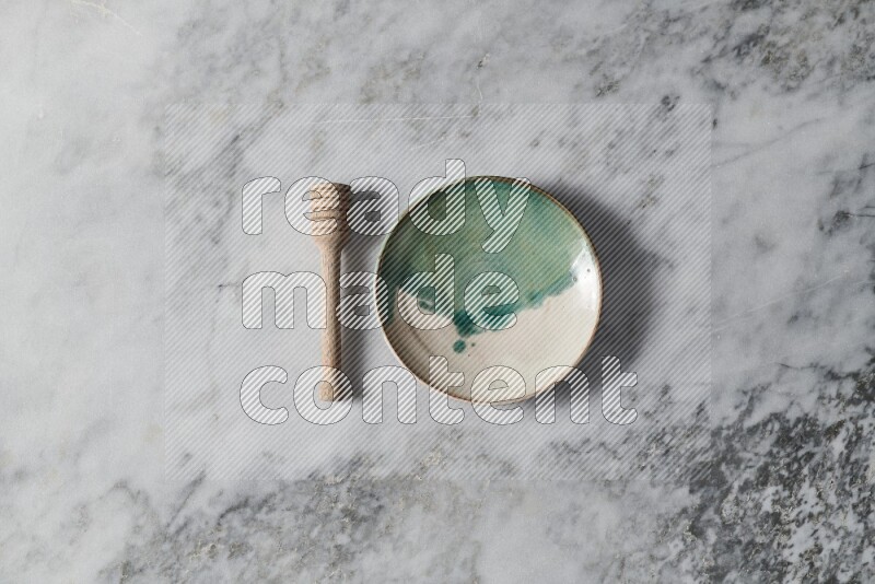 Multicolored pottery plate with wooden honey dipper on the side on grey marble background