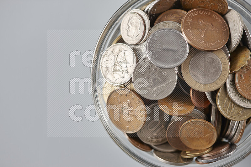 Random old coins in a glass bowl on grey background