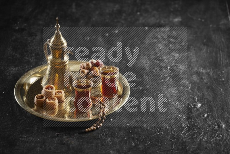 Oriental sweets with dates and a drink on a metal tray in a dark setup
