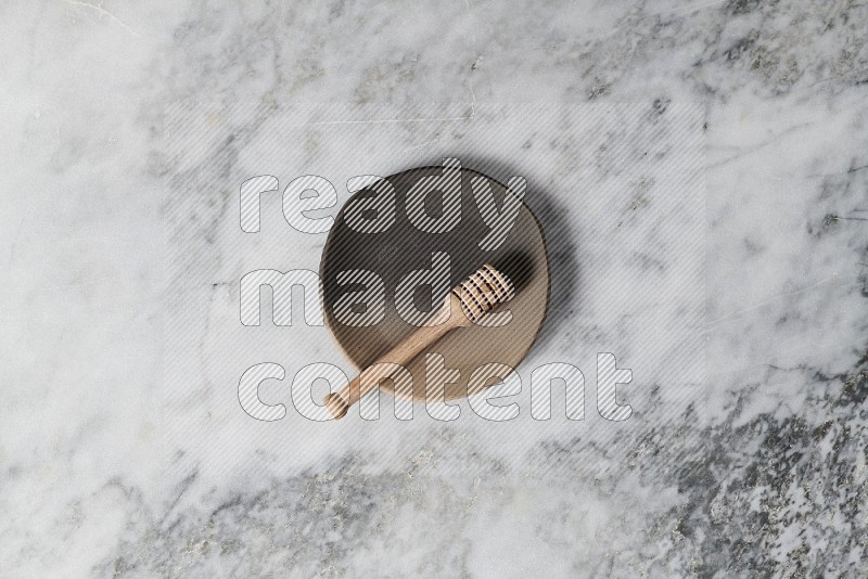 Multicolored Pottery Plate with wooden honey handle in it, on grey marble flooring, Top View