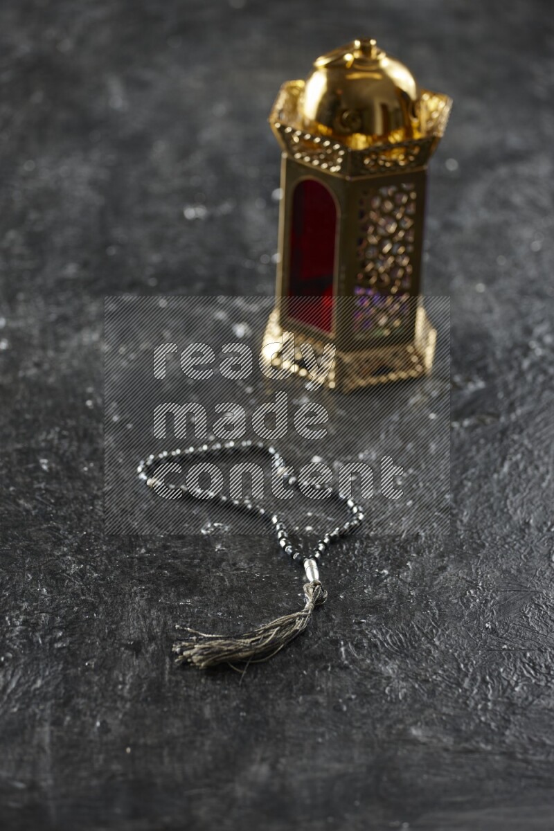 A golden lantern with different drinks, dates, nuts, prayer beads and quran on textured black background