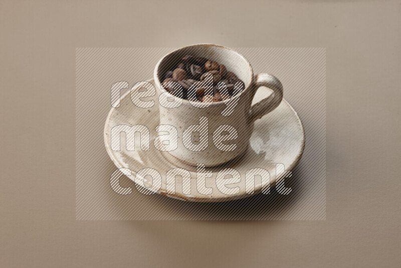 A beige pottery cup full of roasted coffee beans on beige background