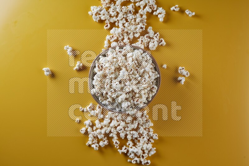 A brown pottery bowl full of popcorn with popcorn beside it on a yellow background in different angles