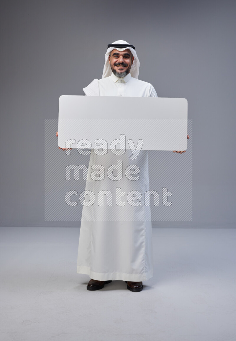 Saudi man Wearing Thob and white Shomag standing holding board on Gray background