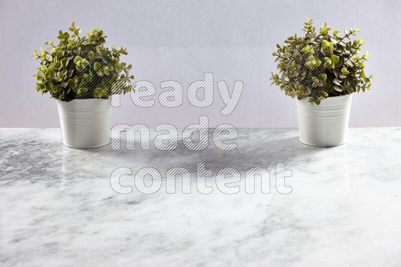 Two green artificial plants in white pot on grey marble background