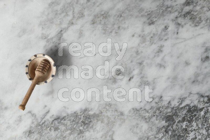 Decorative pottery bowl with wooden honey dipper in it on grey marble background