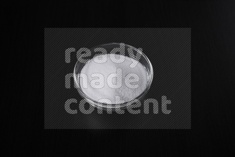 A glass bowl full of fine table salt on black background