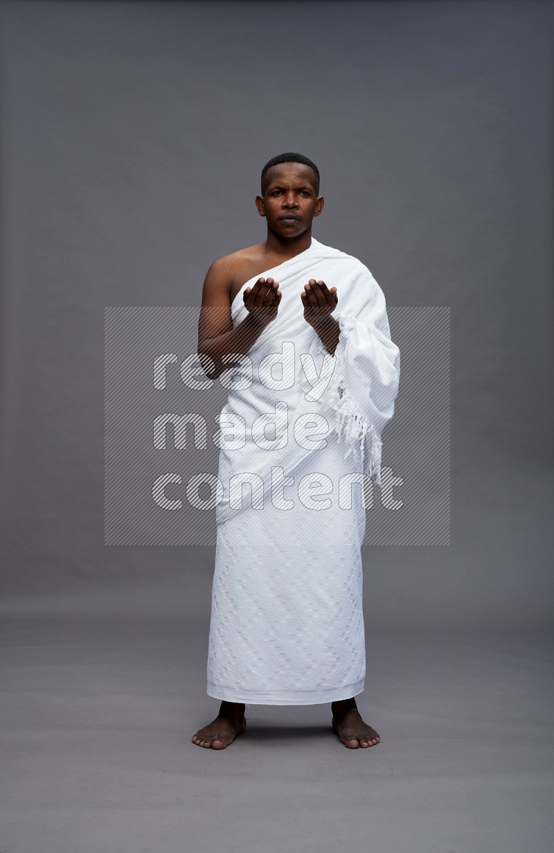 A man wearing Ehram Standing dua'a on gray background