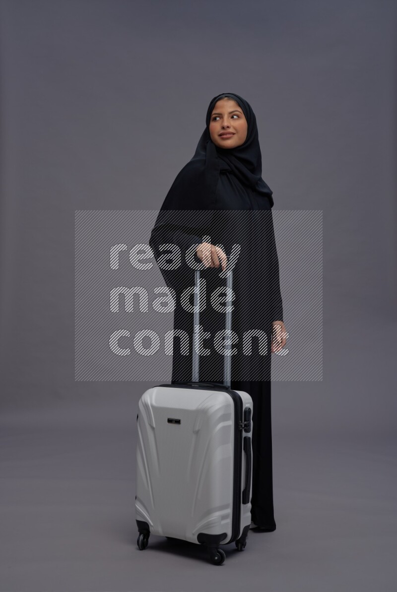 Saudi woman wearing Abaya standing holding bag on gray background