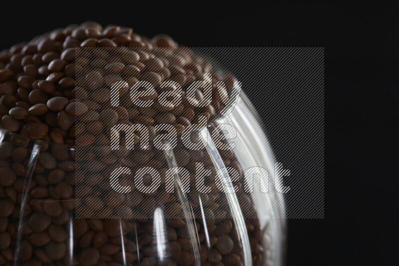 Brown lentils in a glass jar on black background