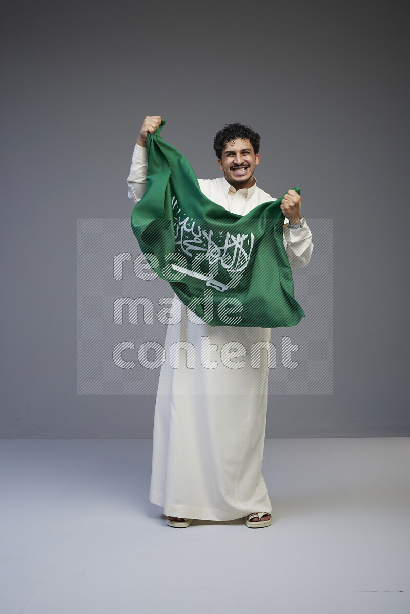 رجل سعودي يرتدي ثوب ابيض ويحمل العلم السعودي