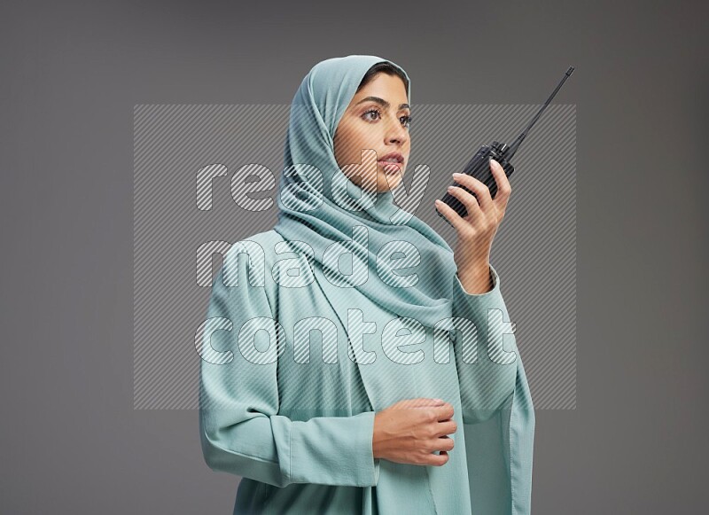 Saudi Woman wearing Abaya standing holding walkie-talkie on Gray background