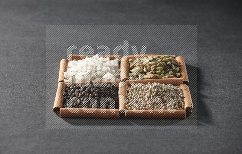 4 مربعات من عيدان القرفة ممتلئة بحبوب الفلفل الأسود والفلفل الأبيض وحب الهيل والملح الأبيض على أرضية سوداء