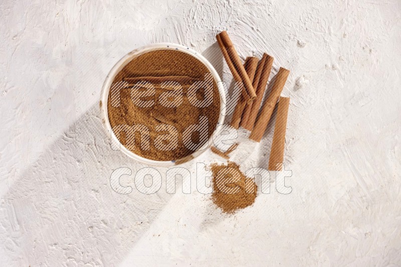 Ceramic bowl full of cinnamon powder with cinnamon sticks on the side on white background