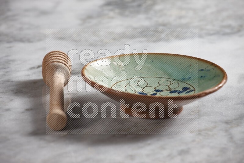 Decorative pottery plate with wooden honey dipper on the side on grey marble background