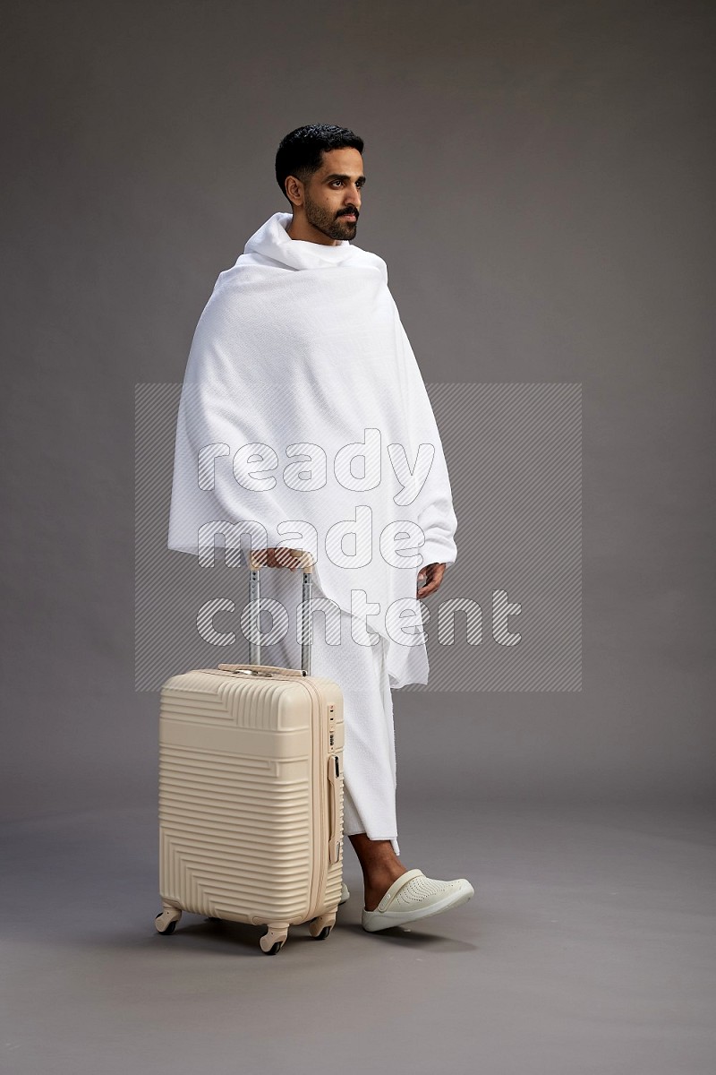 A man wearing Ehram Standing holding traveling bag on gray background