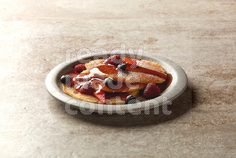 Three stacked mixed berries pancakes in a grey plate on beige background