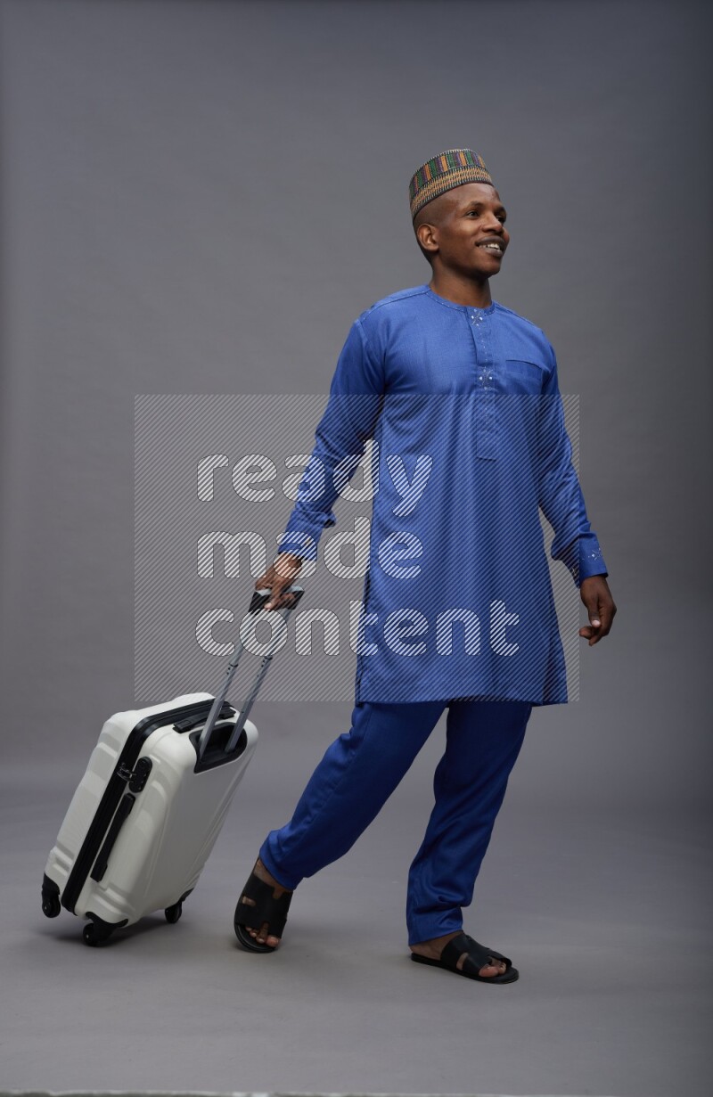 Man wearing Nigerian outfit standing holding bag on gray background