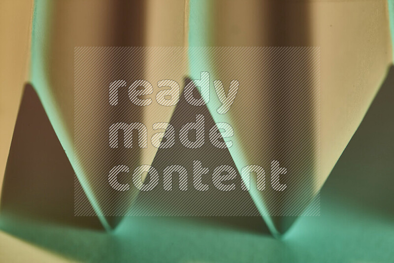 صورة مجردة مقربة تظهر طيات ورقية هندسية حادة بتدرجات اللون الأخضر مع درجات لونية دافئة