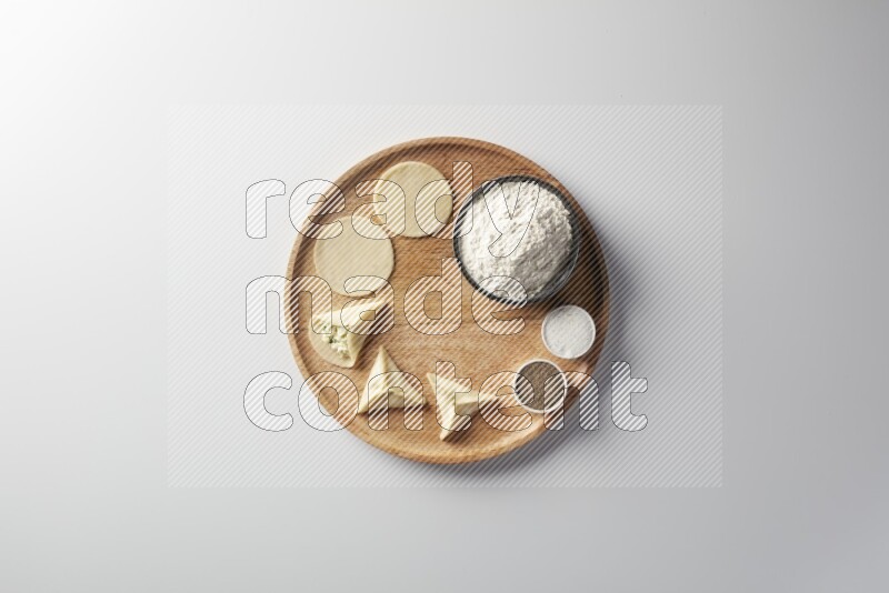 two closed sambosas and one open sambosa filled with cheese while flour, salt, and black pepper aside in a wooden dish on a white background