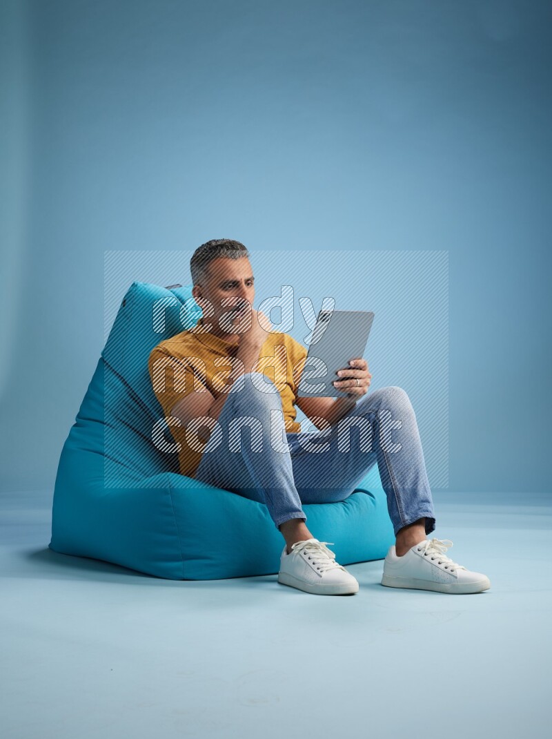 A man sitting on a blue beanbag and working on tablet
