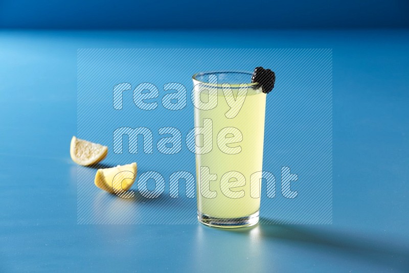 glass of lemon juice with berry on blue background