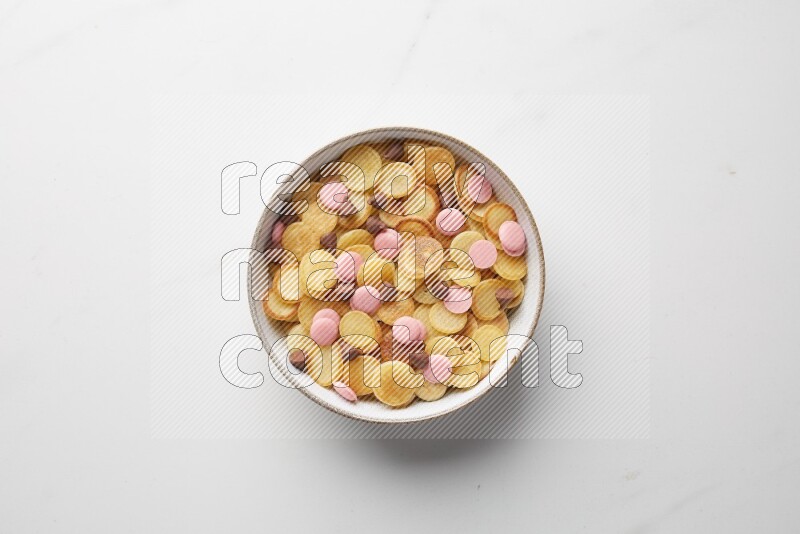 Top-view shot of mixed chocolate chips cereal pancakes in a round bowl on white background
