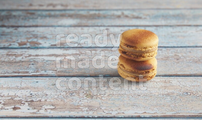 45º Shot of two Yellow Crème Brulée macarons on light blue wooden background