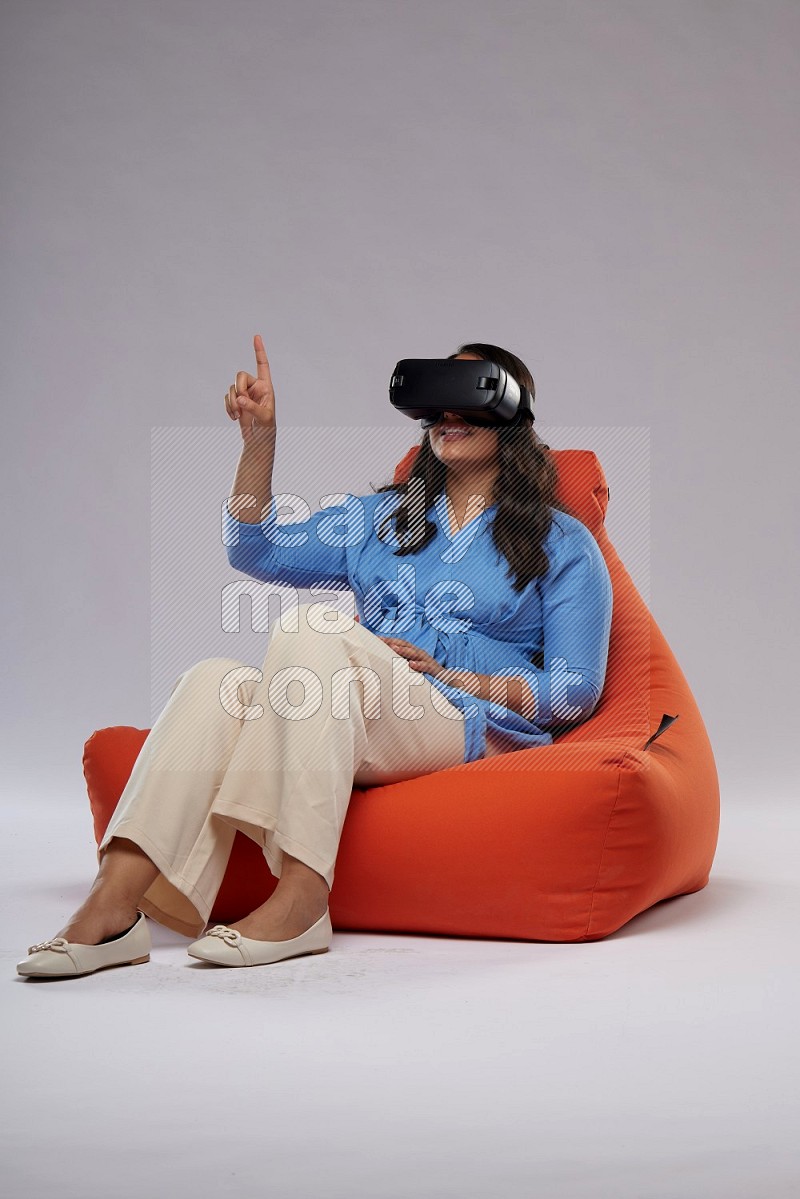 A woman sitting on an orange beanbag and gaming with VR