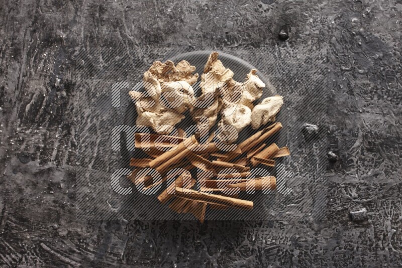 Ginger and cinnamon sticks on a black plate on textured black background